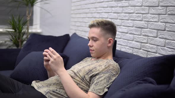 Young Man Playing Mobile Game Using Phone Relaxing on Sofa at Home