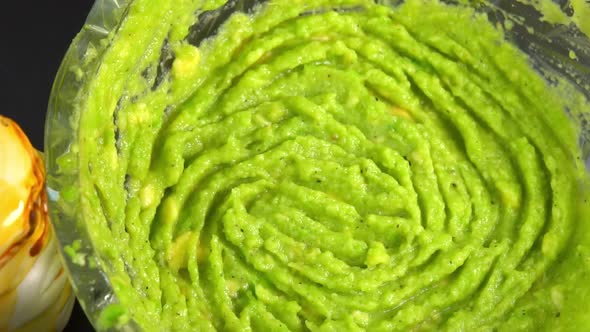 Green guacamole dip rotating in glass bowl background. Cooking healthy food. Making avocado dip