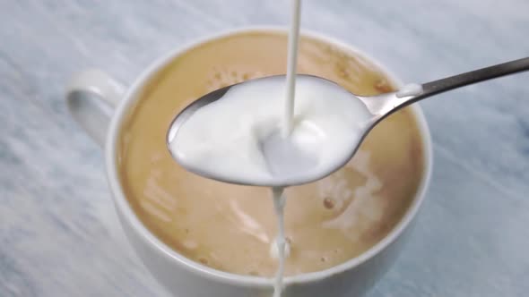 Cold milk splashes into a teaspoon and pours into a hot espresso coffee cup