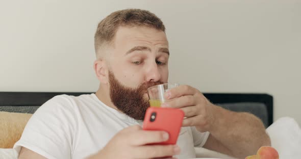 Close Up View of Bearded Young Man Choking on Juice While Reading Shocking News on Smartphone