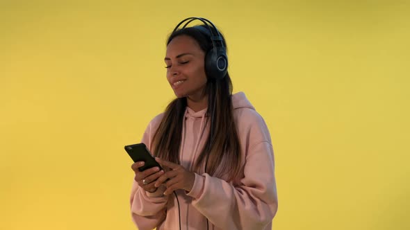 Happy Multiethnic Woman Listening To the Music in Headphones on Yellow Background