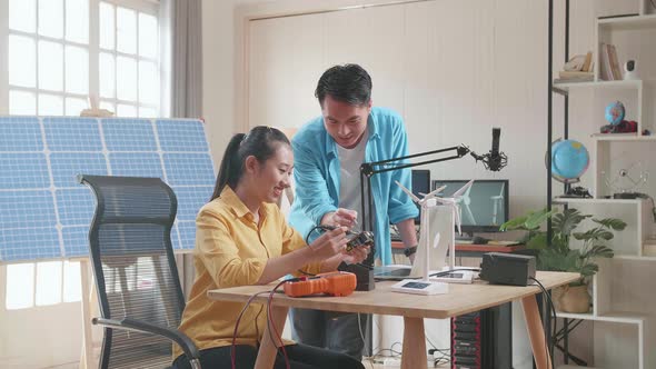 Asian Man Helping Woman Fix The Circuit Board While Working With Laptop Next To The Solar Cell