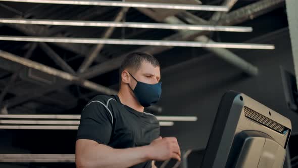 Portrait of an Inflated Athletic Man Running on a Treadmill in a Protective Mask