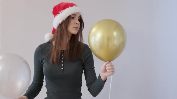 Young Female Green Shirt and Red Santa Hat Holding White and Golden Balloons