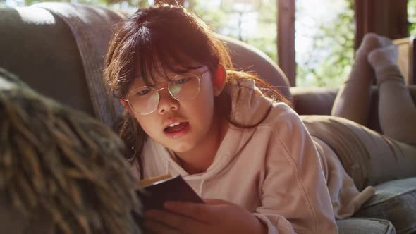 Asian girl smiling while reading a book while siting on the couch at home