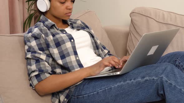 A Woman Works at Home Online and Listens to Music in Large White Headphones