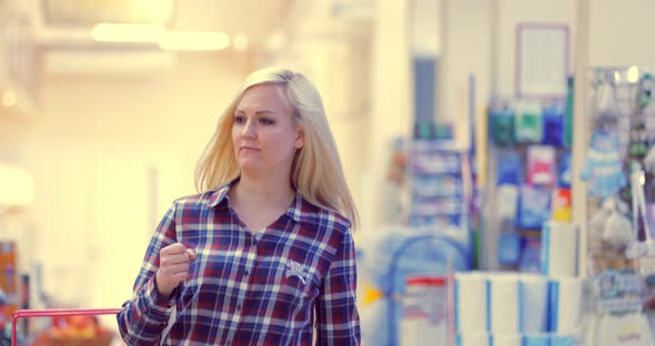 Attractive Woman is Walking Near the Supermarket Shelf and Selects the Products