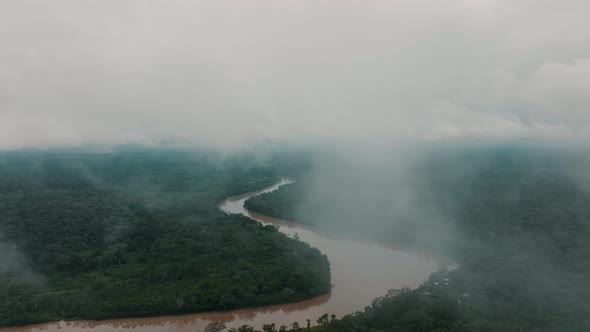 Drone flight between clouds over dense jungle of Peru with brown colored Amazon River