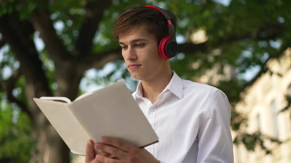 Portrait of Handsome Brunette Young Man Reading Book Memorizing Studying Outdoors on Sunny Day