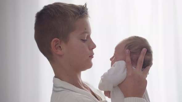 Side View Closeup Teenage Boy Kissing Nose of Infant Girl Indoors at Window