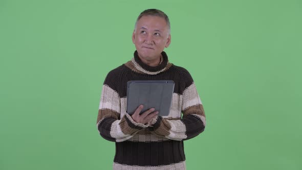 Happy Mature Japanese Man Thinking While Using Digital Tablet and Talking