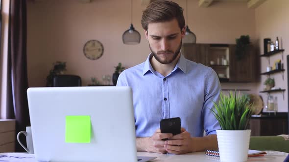 Confident businessman holding smartphone texting message in home office