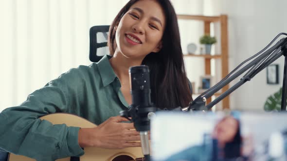 Asia girl influencer play guitar music use microphone record with smartphone for online audience.