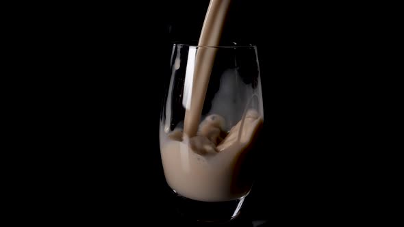 Delicious creamy hazelnut milk poured into a glass in slow motion. Black studio background.