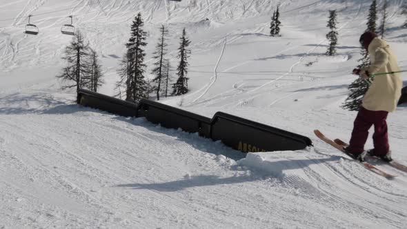 A young man skier performing grind tricks in terrain park.