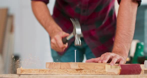 Close Up of Hammering a Nail Into Board A Carpenter Wearing a Red Flannel Shirt Jeans and Cloth