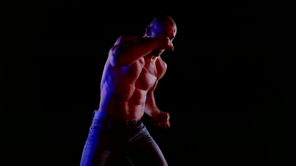 a Muscular Bald Man with a Bare Torso and Jeans Strikes Side and Bottom Blows on a Black Background