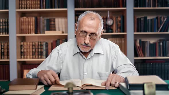 Confident Mature Man Lawyer Reading Educational Book Preparing Defense in Court Public Library Desk