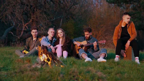 Company of young friends having picnic near bonfire