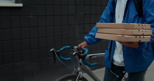 Crop View of Male Courier Carrying Carton Packaging Pizza Boxes and Pushing Bike