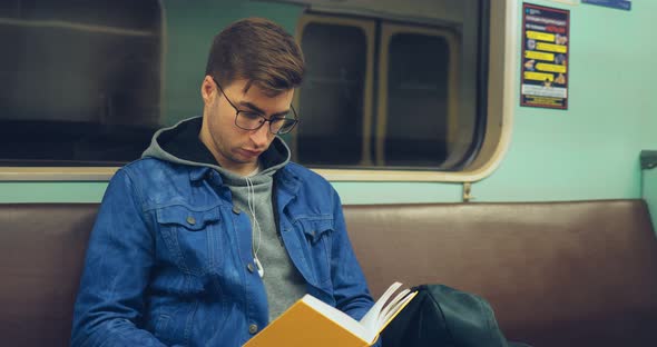 Brutal Guy with Glasses Riding in a Subway Car and Reading a Book with Interest