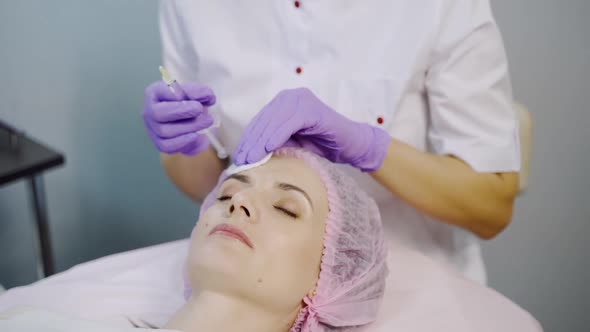 specialist is making injections of mesotherapy to a client in the forehead area