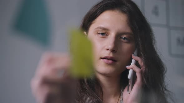 Closeup of Confident Serious Concentrated Caucasian Woman Talking on Phone Writing on Sticky Notes