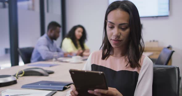 Portrait of smiling biracial businesswoman using tablet looking at camera in modern office