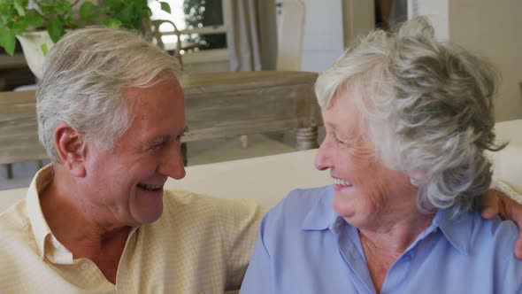 Caucasian senior couple smiling while looking at each other sitting on the couch at home