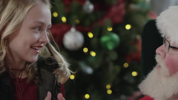 Santa hands girl a candy cane as they talk