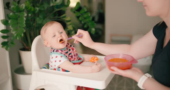 Little baby girl eating baby food on high chair with mother