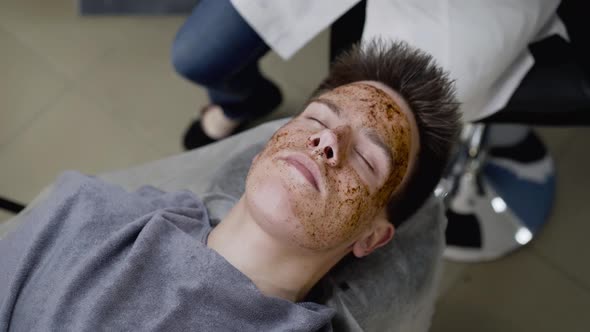 View of Beautician's Hands Wipe a Coffee Scrub From the Man's Face with Sponge