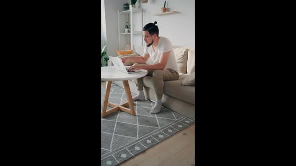 Young Man Using Laptop Typing and Working Sitting on the Couch at Home Vertical Video