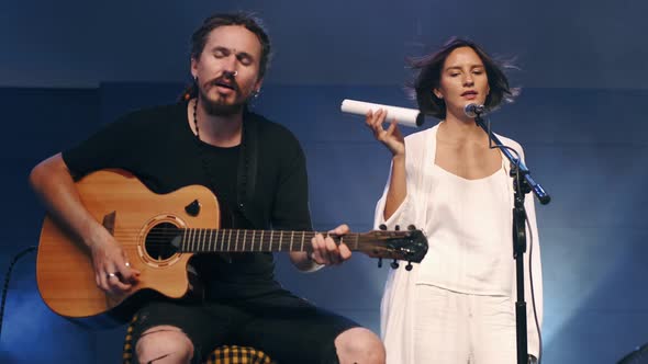 Female Singer with Shaker and Musician Playing Guitar Performing on Stage