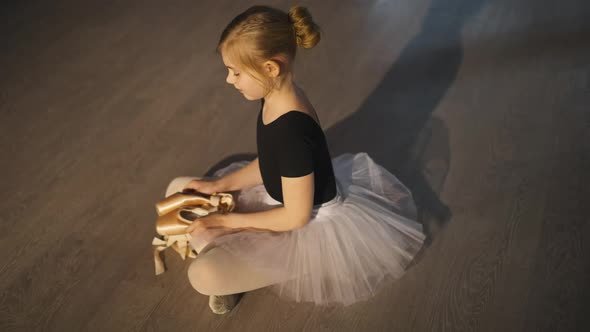 High Angle View of Smiling Happy Ballet Student Sitting on Floor Admiring New Pointe Shoes