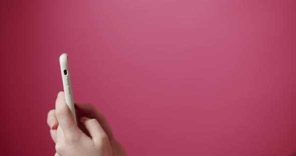 Woman's Hands Use a White SmartPhone on an Isolated Pink Background