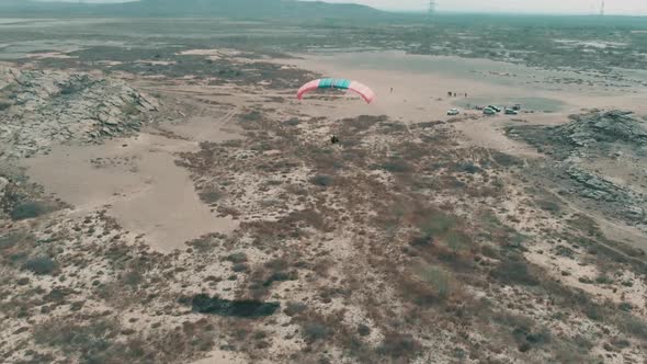 Aerial View Of Flying Motorised Paraglider Flying Over Sandy Rocky Desert Landscape. Follow Shot