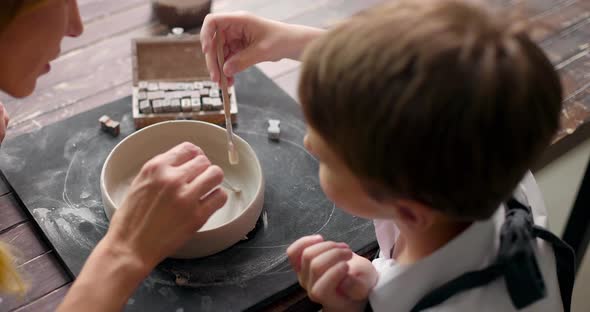 Mother and Son Boy Adorn a Clay Bowl with Letters Together