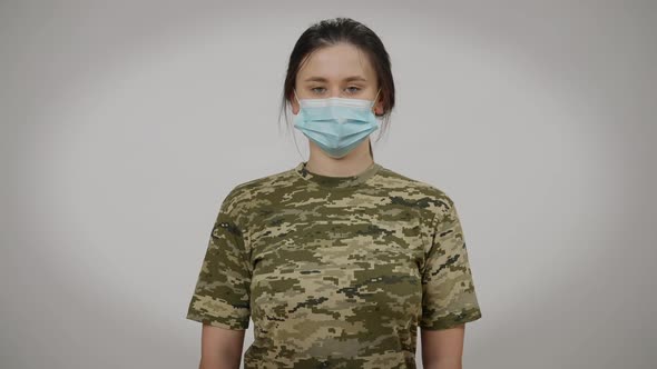 Front View Portrait of Serious Young Military Woman in Coronavirus Face Mask Posing at Grey