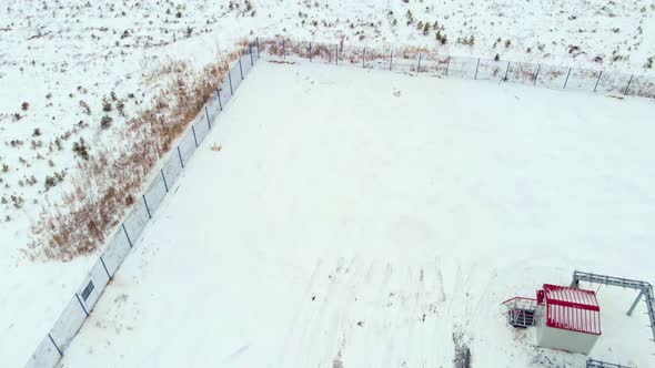 A Small Tractor Loader Cleans Snow Near Buildings of Oil and Gas Equipment