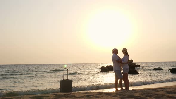 Honeymoon. Romantic Couple of Lovers, Silhouettes. Travelers Stand on Beach, Hug and Kiss Against