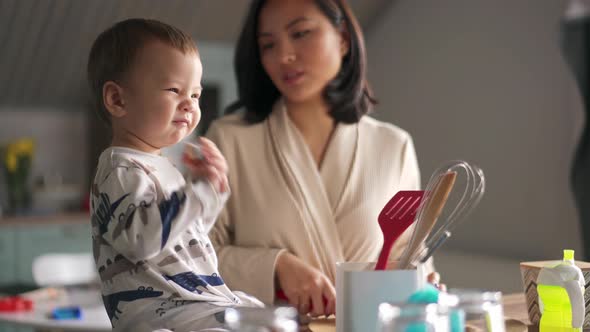 Positive Asian mom slicing something while her baby is playing with spoon