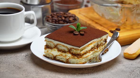 Traditional Italian Tiramisu dessert in glass baking dish and portion on grey concrete background