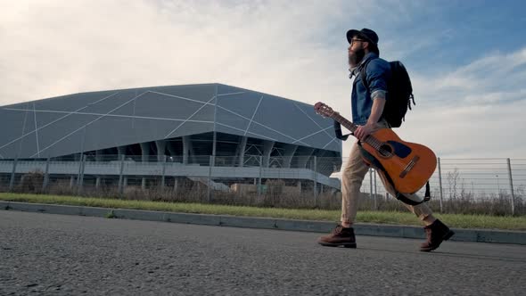 Guy with a Guitar Hiker. He Is on the Road at Sunset.