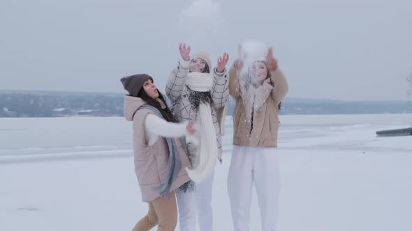 Group of three happy women having fun and playing with snow in winter park.