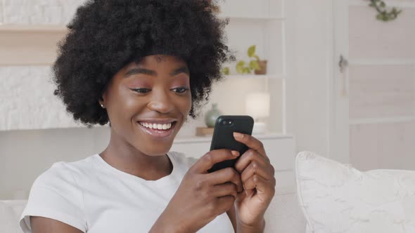 Smiling African American Millennial Woman Holding Smartphone Having Fun Playing Mobile Games Enjoy