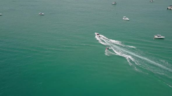 Tracking aerial: man on red surfboard waterskies on green lagoon water