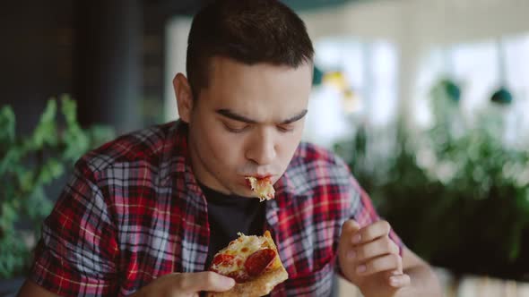 man in a plaid shirt is eating delicious pizza at a pizzeria in the afternoon