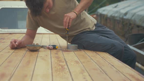 Carpenter unscrewing screws around vent on roof of wooden boat