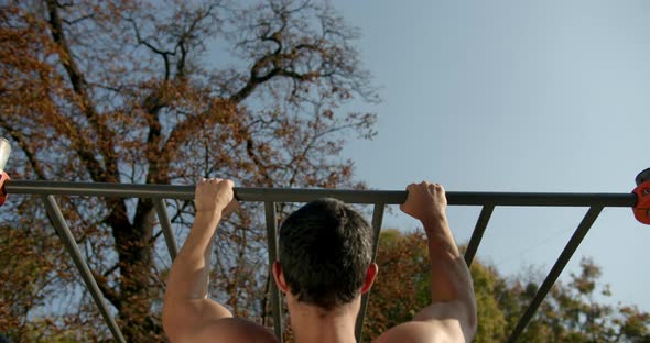 Young Man Is Doing Pull Ups on the Bar in Sunny Weather 